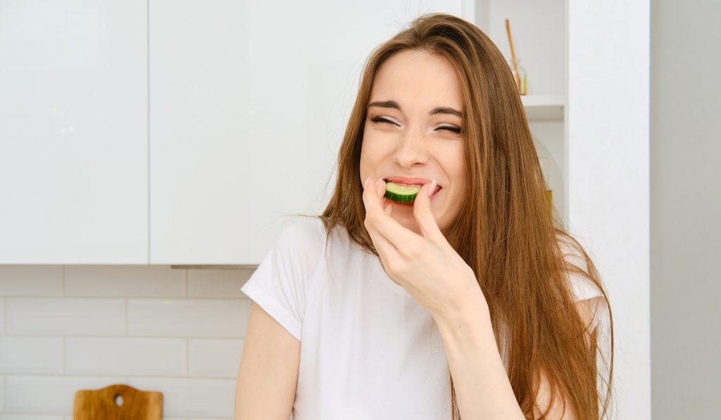 happy young woman biting cucumber