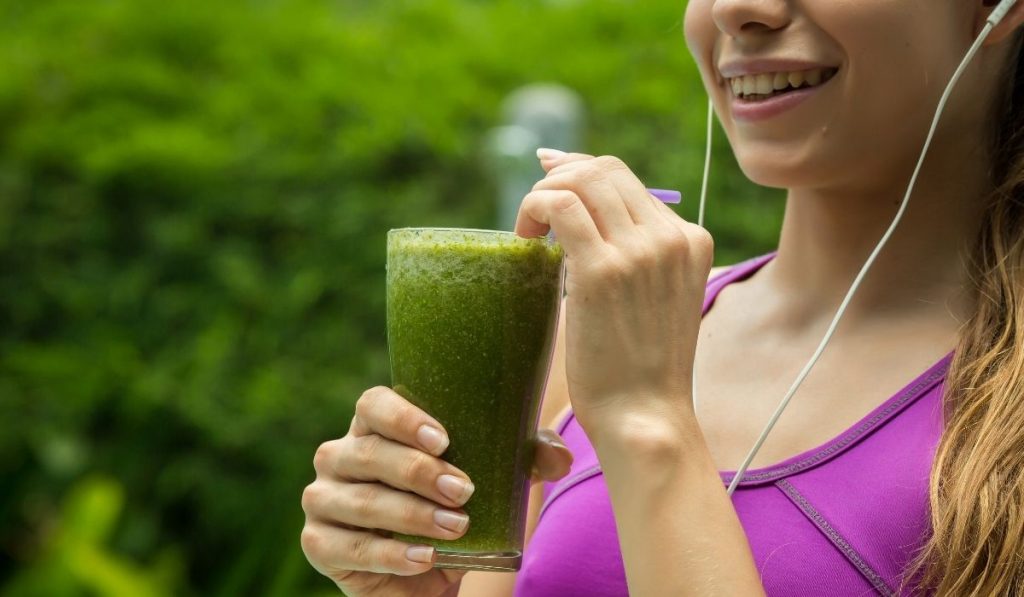 athletic girl with earphones holding a glass of green juice - ss220324