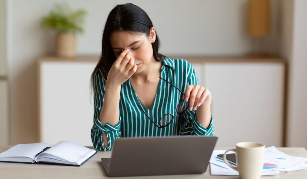 woman having eyes fatigue massaging her nose bridge at work
