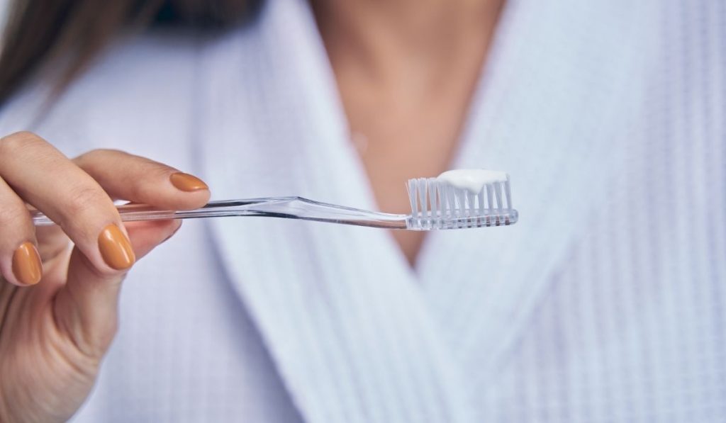 woman wearing a robe holding a toothbrush with a toothpaste - ee220401